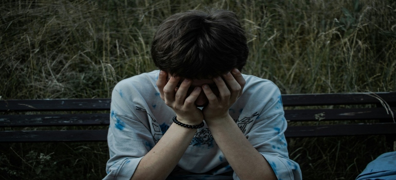 A young person sits on a bench, thinking about why self-harm and substance abuse often go together